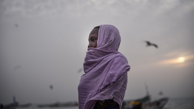 Foto seitenansicht einer frau mit schal, die während des sonnenuntergangs am strand gegen den himmel steht