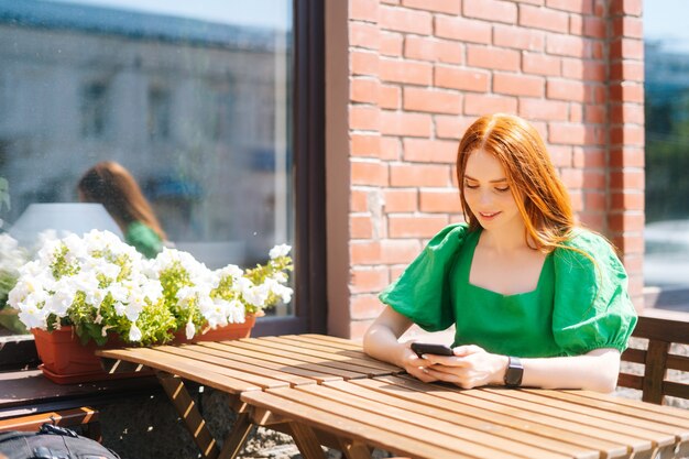 Seitenansicht einer glücklichen jungen Frau, die auf der Terrasse des Cafés im Freien am Tisch sitzt