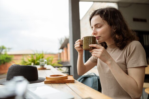 Seitenansicht einer glücklichen schönen Dame, die ein heißes Getränk im Café im Freien genießt