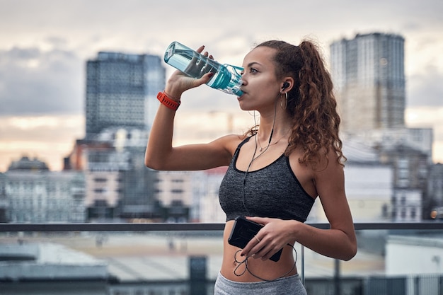 Seitenansicht einer jungen athletischen Frau, die Wasser aus Sportflaschen trinkt