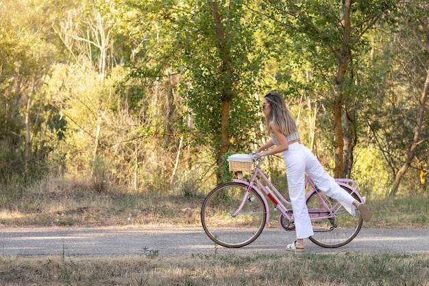 Seitenansicht einer jungen eleganten Frau, die im Frühling mitten in der Natur auf ein rosafarbenes Retro-Fahrrad steigt