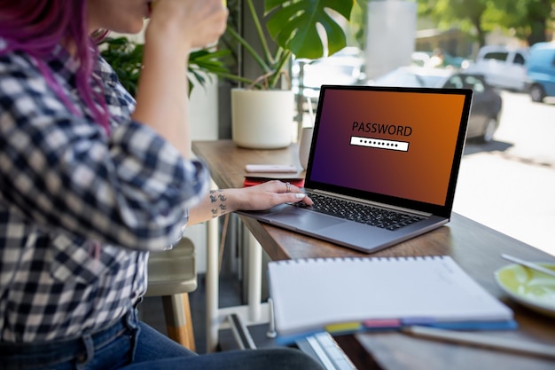 Seitenansicht einer jungen Frau mit rosa Haaren, die im Café sitzt und Laptop-Computer mit Passwort-Login schreibt...