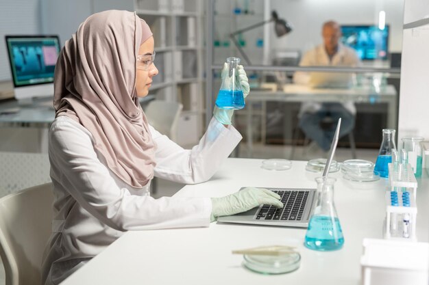 Seitenansicht einer jungen muslimischen Wissenschaftlerin im Hijab mit Reagenzglas