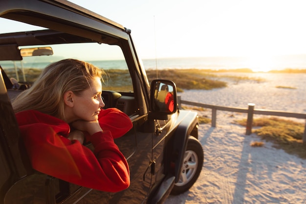 Seitenansicht einer kaukasischen Frau in einem offenen Auto, die durch das Fenster schaut. Wochenend-Strandurlaub, Lifestyle und Freizeit.