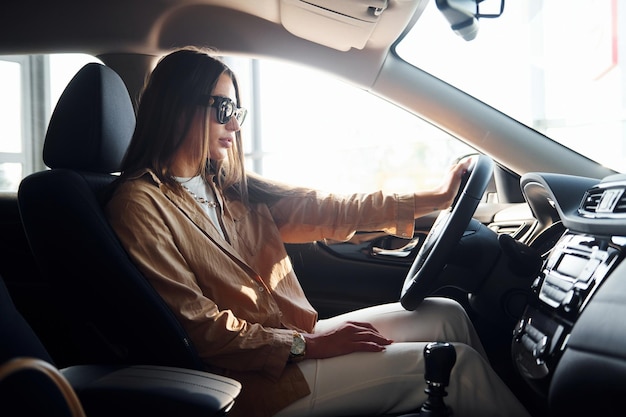 Seitenansicht einer modischen, schönen jungen Frau, die sich in ihrem modernen Automobil befindet