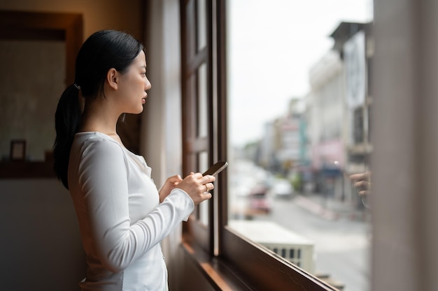 Seitenansicht einer nachdenklichen asiatischen Frau, die aus dem Fenster schaut und etwas in ihrem Kopf denkt