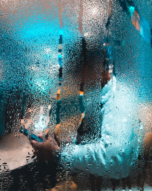 Foto seitenansicht einer person, die ein telefon benutzt, gesehen durch ein nasses fenster