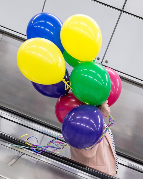 Foto seitenansicht einer person, die farbenfrohe ballons hält, während sie auf einer rolltreppe steht