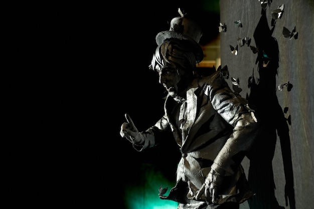 Seitenansicht einer professionellen Pantomime, die ausdrucksstarke Emotionen zeigt, gekleidet wie eine Bronzestatue mit vielen künstlichen Schmetterlingen, die ihn für Anzug und Hut zu ziehen scheinen. Männlicher Künstler, der auf der Bühne auftritt