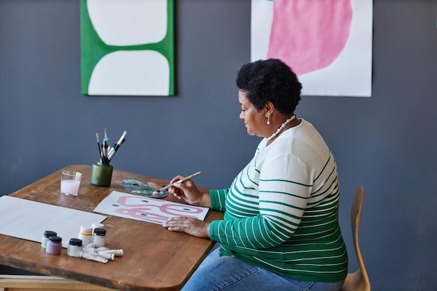 Seitenansicht einer Rentnerin mit Pinsel, die im Atelier neue Kunstwerke schafft