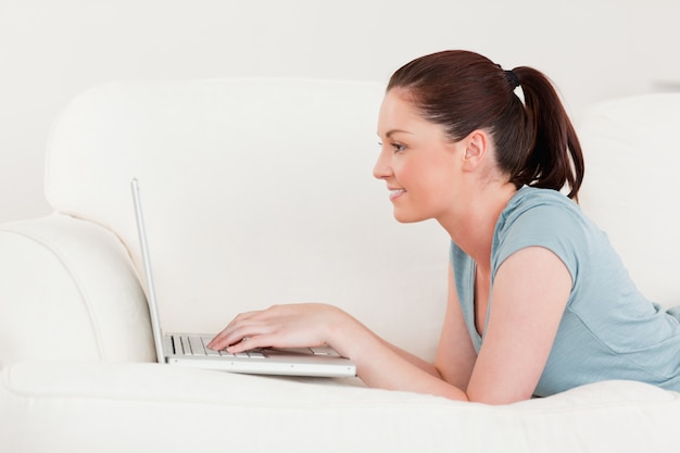 Seitenansicht einer schönen Frau, die mit ihrem Laptop beim Lügen auf einem Sofa sich entspannt