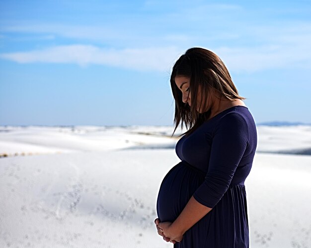 Seitenansicht einer schwangeren Frau, die am Strand gegen den Himmel steht