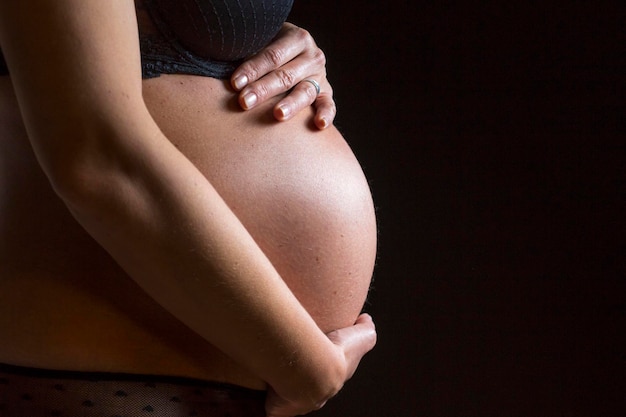 Seitenansicht einer schwangeren Frau, die ihren Bauch gegen schwarzen Hintergrund berührt