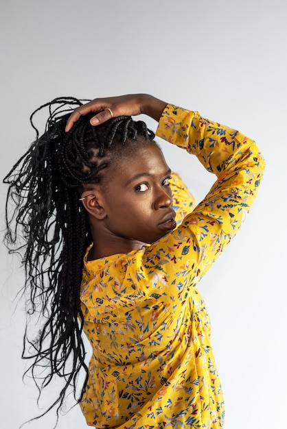 Seitenansicht eines afroamerikanischen weiblichen Modells mit Zöpfen, die Haare berühren, während sie die Kamera auf grauem Hintergrund im Studio betrachten