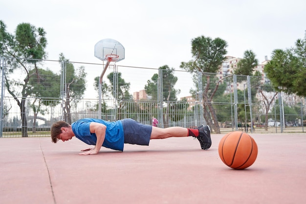 Seitenansicht eines athletischen jungen Mannes, der Liegestütze mit einem Basketballplatz macht