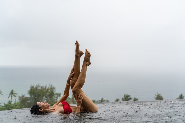 Seitenansicht eines attraktiven Mädchens, das an einem regnerischen Tag in einem Infinity-Pool liegt