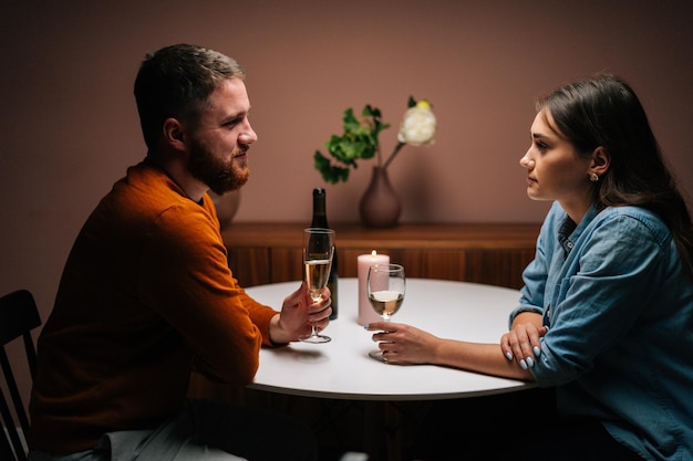 Seitenansicht eines glücklichen romantischen jungen Paares, das es genießt, sich zu unterhalten und zusammen am Esstisch mit Kerzen in einem dunklen Raum zu sitzen. Liebe Mann und Frau feiern Jubiläum, Valentinstag zu Hause.