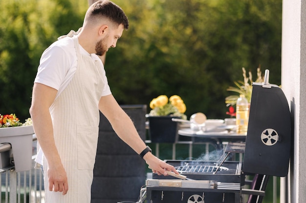 Seitenansicht eines gutaussehenden Mannes, der versucht, wie heiß der Grill ist, Mann in Schürze, der das Abendessen im Freien zubereitet