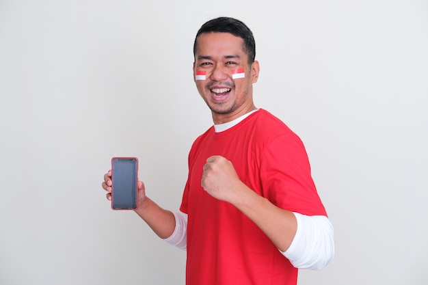 Seitenansicht eines Indonesiers, der mit aufgeregter Geste einen leeren Handy-Bildschirm zeigt