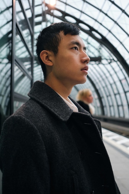 Seitenansicht eines jungen asiatischen Geschäftsmannes, der nachdenklich auf den Zug an der U-Bahnstation wartet