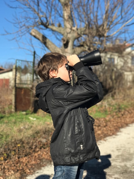 Foto seitenansicht eines jungen, der durch ein fernglas auf der straße steht