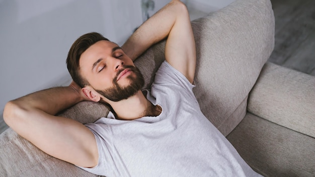 Seitenansicht eines jungen gutaussehenden bärtigen Mannes in Freizeitkleidung, der zu Hause auf der Couch schläft oder entspannt