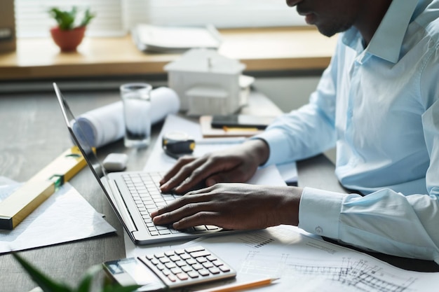 Seitenansicht eines jungen männlichen Architekten, der am Schreibtisch sitzt und auf der Laptop-Tastatur tippt