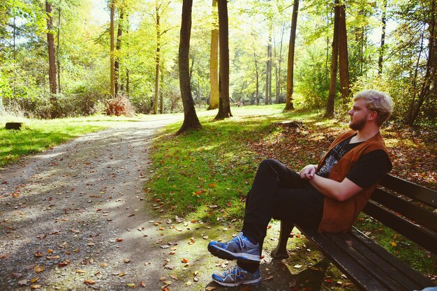 Foto seitenansicht eines jungen mannes, der auf einer bank im wald sitzt