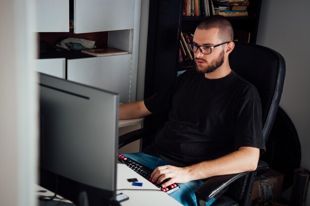 Foto seitenansicht eines jungen mannes, der zu hause auf einem stuhl einen computer benutzt