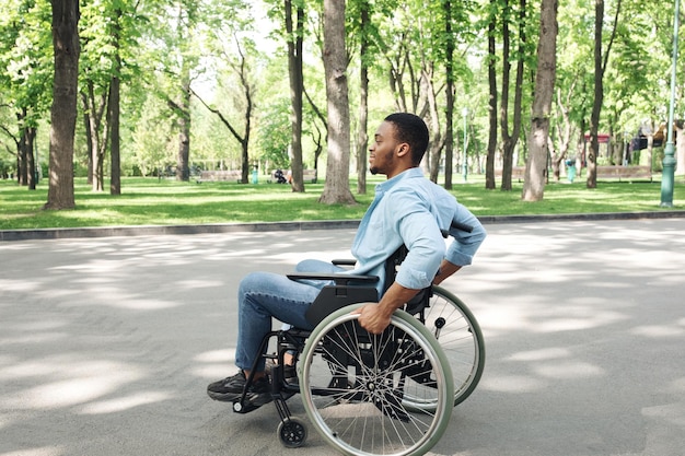 Seitenansicht eines jungen Schwarzen im Rollstuhl, der Zeit im Stadtpark in voller Länge verbringt