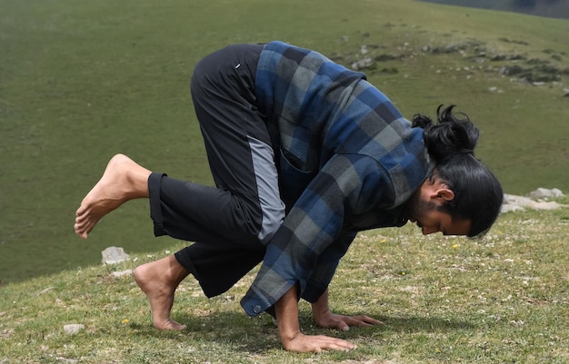 Foto seitenansicht eines jungen wanderers, der versucht, die bakasana-yoga-pose in der natur zu machen