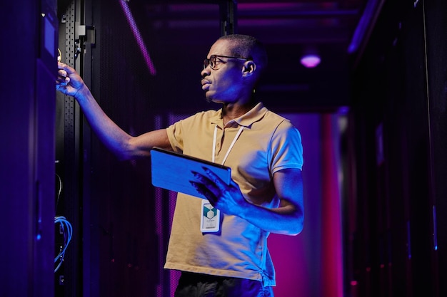 Seitenansicht eines männlichen Systemadministrators, der ein Servernetzwerk in einem von Neonlicht beleuchteten Rechenzentrum einrichtet