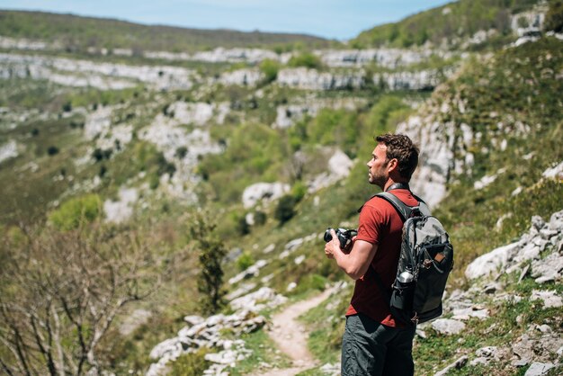 Seitenansicht eines männlichen Wanderers mit Rucksack, der auf einer felsigen Klippe steht und die Anzeige der Fotokamera betrachtet