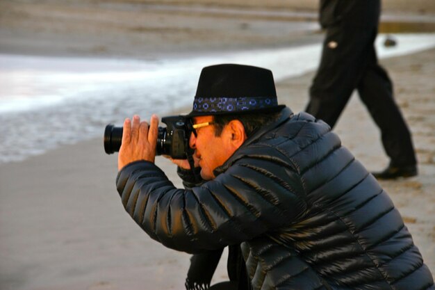 Seitenansicht eines Mannes, der am Strand mit einer Kamera fotografiert