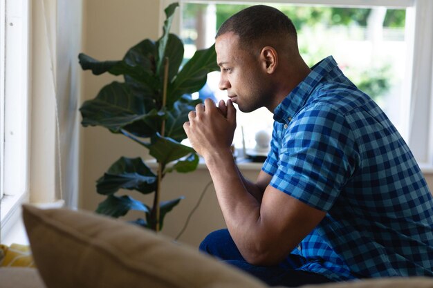 Foto seitenansicht eines nachdenklichen jungen afroamerikanischen mannes, der zu hause mit den händen am kinn sitzt. konzept von menschen und emotionen, unverändert.