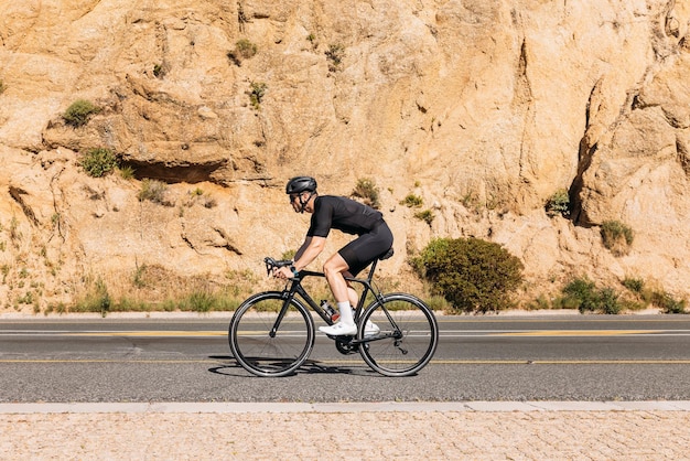 Seitenansicht eines professionellen Radfahrers in schwarzer Sportbekleidung, der am Berg Fahrrad fährt