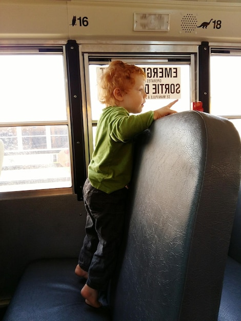 Foto seitenansicht eines süßen jungen, der auf einem sitz im schulbus steht