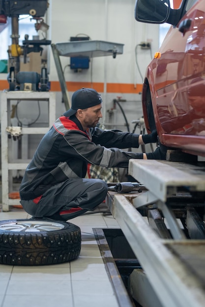 Seitenansicht in voller Länge Porträt eines männlichen Mechanikers, der Reifen am Auto wechselt, während er in der Autowerkstatt arbeitet