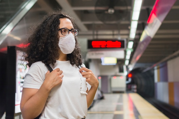 Foto seitenansicht junge frau mit medizinischer maske, die auf die u-bahn wartet