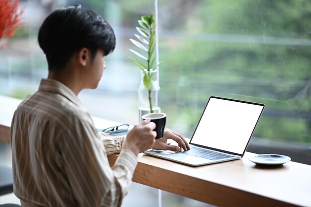 Seitenansicht junger Mann, der Kaffeetasse hält und mit Laptop-Computer im Café arbeitet.