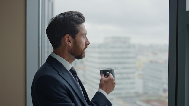 Seitenansicht nachdenklicher Geschäftsmann, der Kaffee am Bürofenster aus nächster Nähe trinkt