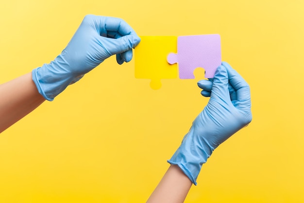 Seitenansicht Nahaufnahme der menschlichen Hand in blauen chirurgischen Handschuhen, die gelbe und violette Puzzlestücke halten.