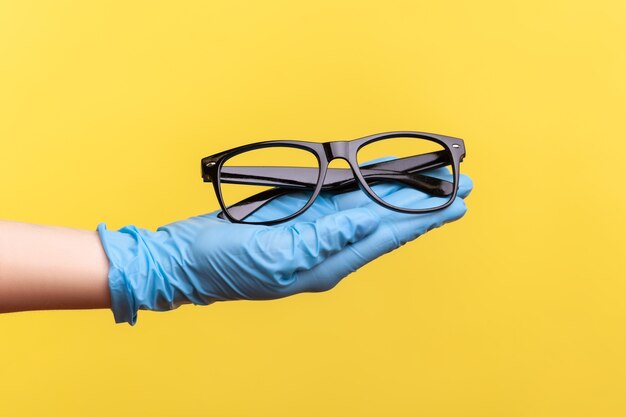 Seitenansicht Nahaufnahme der menschlichen Hand in blauen chirurgischen Handschuhen, die schwarzen Brillenrahmen halten und geben.