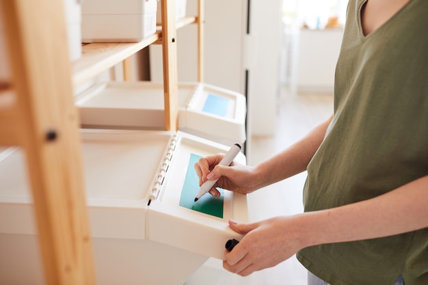 Seitenansicht Nahaufnahme der nicht erkennbaren Frau, die Plastikbehälter zu Hause kennzeichnet, während Lagerung und Müllsortierung zu Hause verwaltet