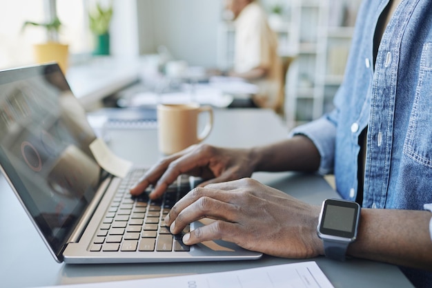 Seitenansicht Nahaufnahme eines afroamerikanischen Mannes, der im Büro arbeitet, mit Fokus auf Händen, die am Laptop ke tippen