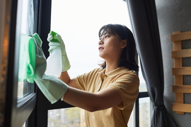 Seitenansicht Porträt einer jungen asiatischen Frau, die zu Hause Fenster putzt, Kopienraum