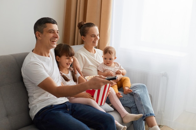 Seitenansicht Porträt einer positiv optimistischen Familie mit ihren Kindern, die zu Hause im hellen Raum auf dem Sofa sitzen und lustige Filme ansehen, die gute Emotionen ausdrücken und lachen