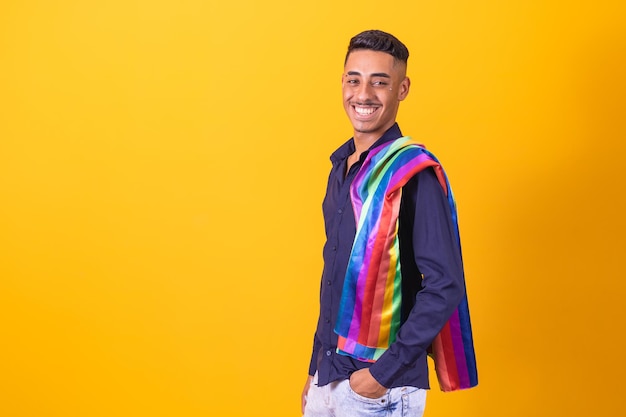 Seitenansicht Porträt eines fröhlichen jungen afroschwarzen lateinamerikanischen Mannes mit einer Gay-Pride-Regenbogenfahne im Studio über gelbem Hintergrund Homosexuelles Konzept Regenbogenfahne feiert Parade Kopierraum