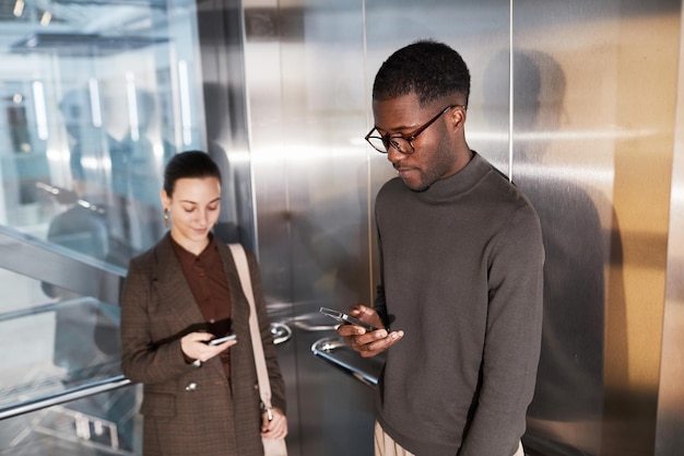 Seitenansicht Porträt eines jungen schwarzen Geschäftsmannes mit Smartphone im Aufzug in einem modernen Bürogebäude
