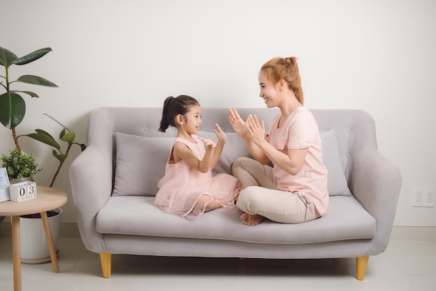 Seitenansicht Porträt eines kleinen Mädchens, das Klatschspiel spielt, während die Mutter zusammen auf dem Sofa sitzt